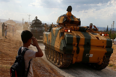 A boy salutes as Turkish Armed Forces vehicles drive pass by a village on the Turkish-Syrian border line in Reyhanli, Hatay province, Turkey October 11,
