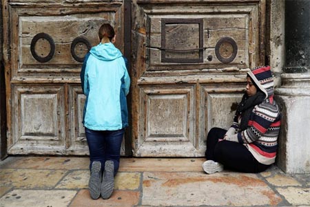 Worshipper sit next to the closed doors of the Church of the Holy Sepulchre in Jerusalem's Old City.
