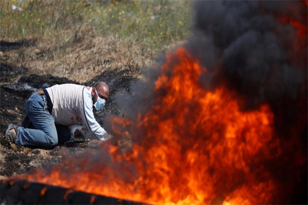 A Palestinian takes cover during clashes with Israeli troops at a protest demanding the right to return to their homeland, at the Israel-Gaza border east of Gaza City, on April 6, 2018.