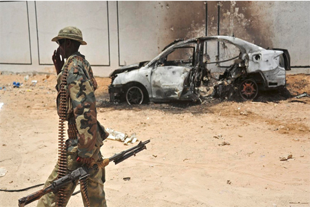 A Somali soldier patrols next to the burnt-out wreckage of a car that was used by suspected al-shabab fighters.