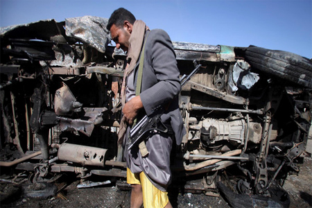 A Houthi stands next to a destroyed vehicle, which belongs to a Houthi man, after an improvised explosive device under it detonated in Sanaa January 25, 2015. (Reuters)