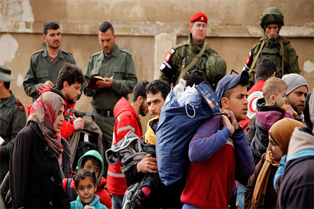 Syrian army soldiers (back L) and Russian soldiers (back R) monitor as rebel fighters and their families evacuate the besieged Waer district in the central Syrian city of Homs, March 18, 2017.